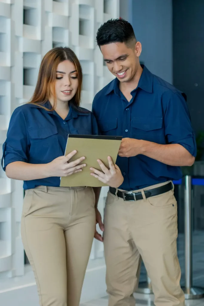 Two colleagues in matching uniforms reviewing documents in a modern office.